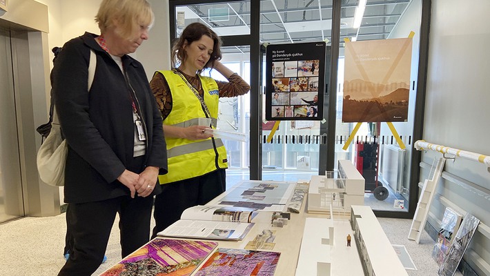 Torunn Skoglund och konstnär Magdalena  Nilsson tittar på konstmaterial under öppet hus vid ny vårdbyggnad.